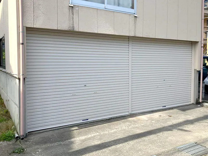 リフォームで新しく交換されたガレージの白い軽量シャッター。住宅外観と2連シャッターの様子。