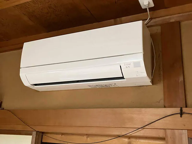 住宅リフォームに伴い、古い和室の壁面に新しく設置された白い三菱電機製エアコン。電気工事を経てすっきりと取り付けられた最新の室内機。
