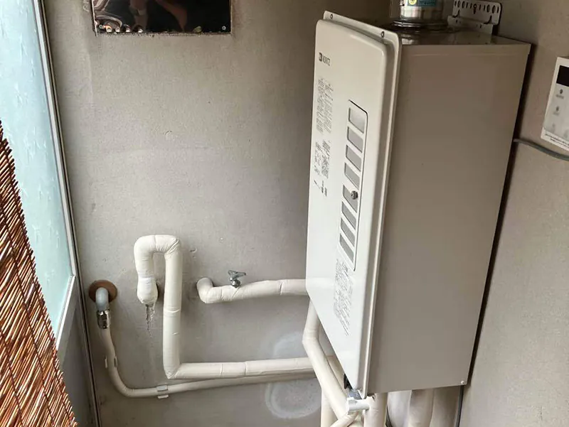 リフォームで新しく交換された壁掛け式のガス給湯器。ノーリツ製の本体から伸びる配管類に、きれいに断熱材が巻き直された設置後の様子。