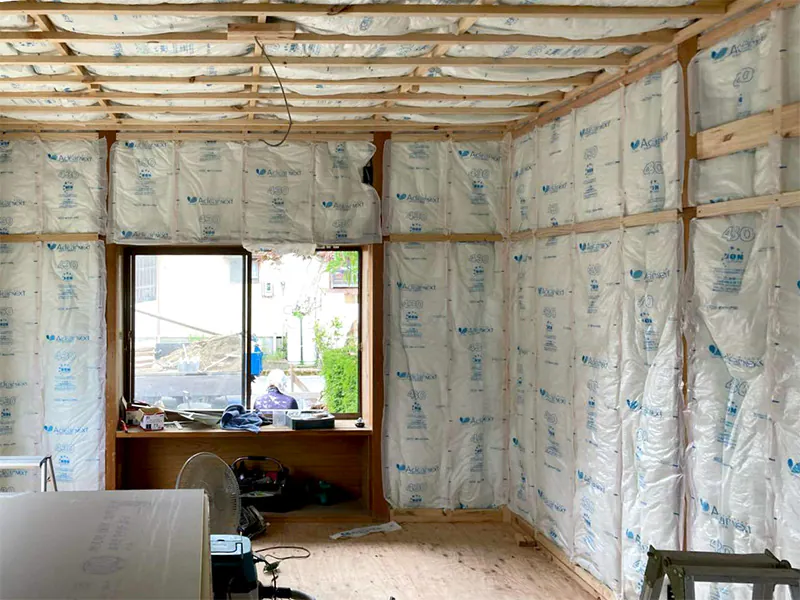 築古住宅リフォームの断熱材施工中(工事中)。壁と天井全体に袋入りグラスウールの断熱材が施され、木造の骨組みがむき出し。