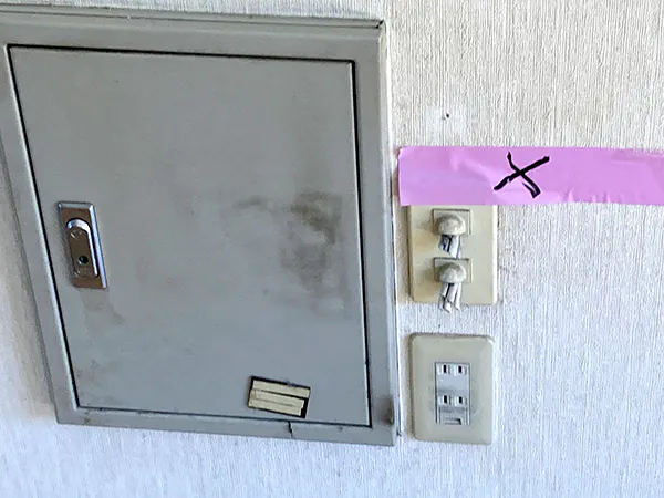 古い分電盤とピンクテープで養生された露出配線の壁面